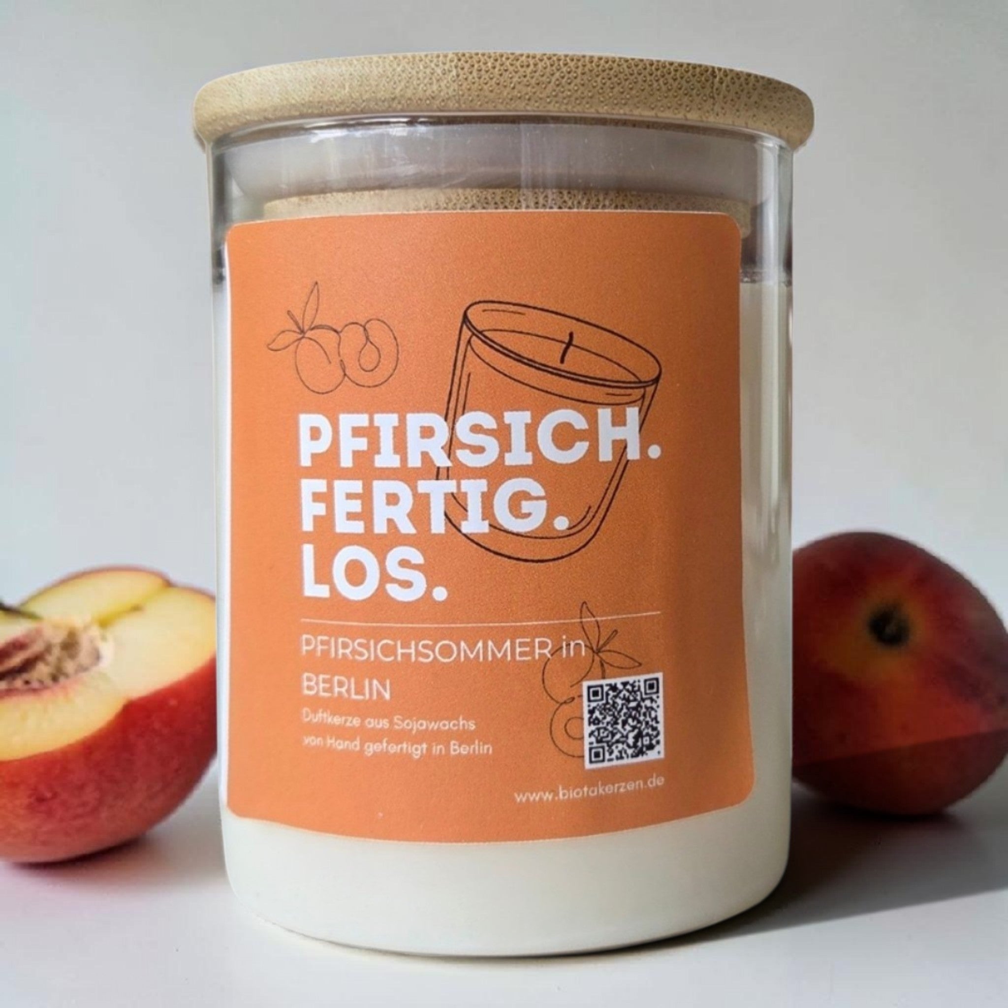 Biotakerzen Pfirsichsommer Berlin Duftkerze aus Sojawachs mit orangem Etikett, frische Pfirsiche im Hintergrund