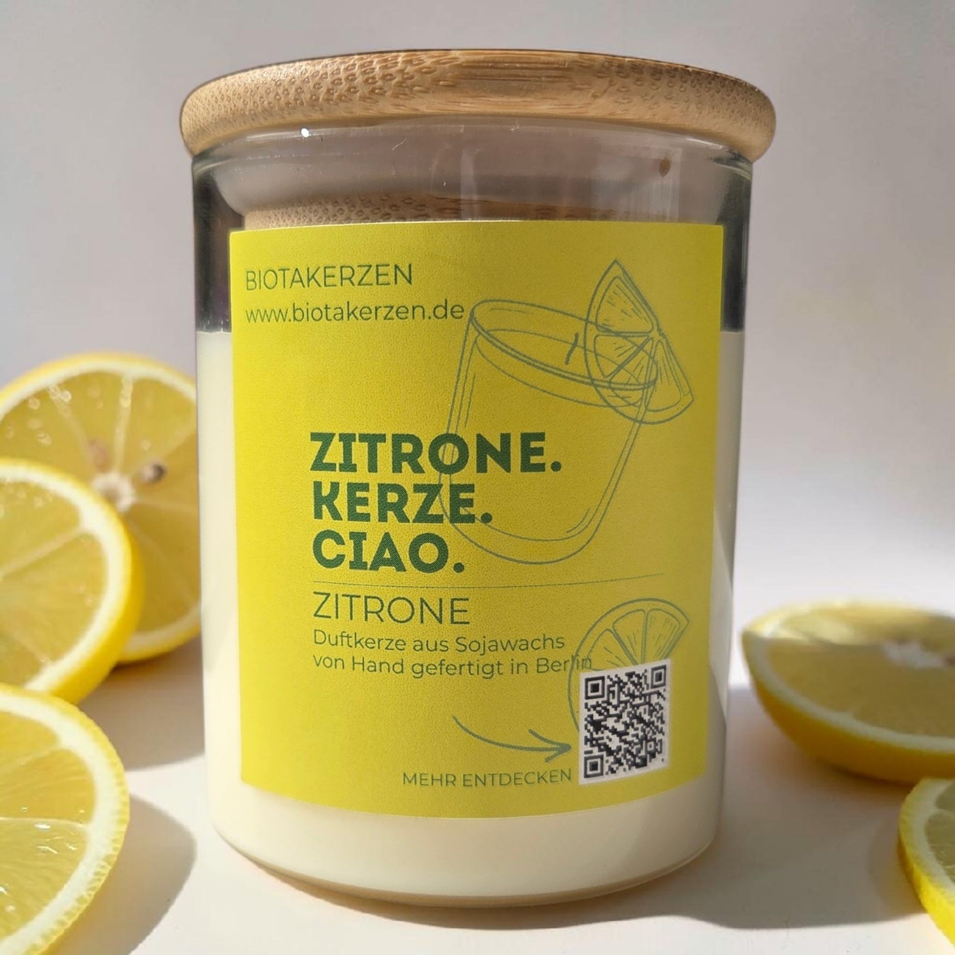 BiotaKerzen Zitrone Duftkerze aus Sojawachs im Glas mit Bambusdeckel und gelbem Etikett, umgeben fron frischen Zitronenscheiben
