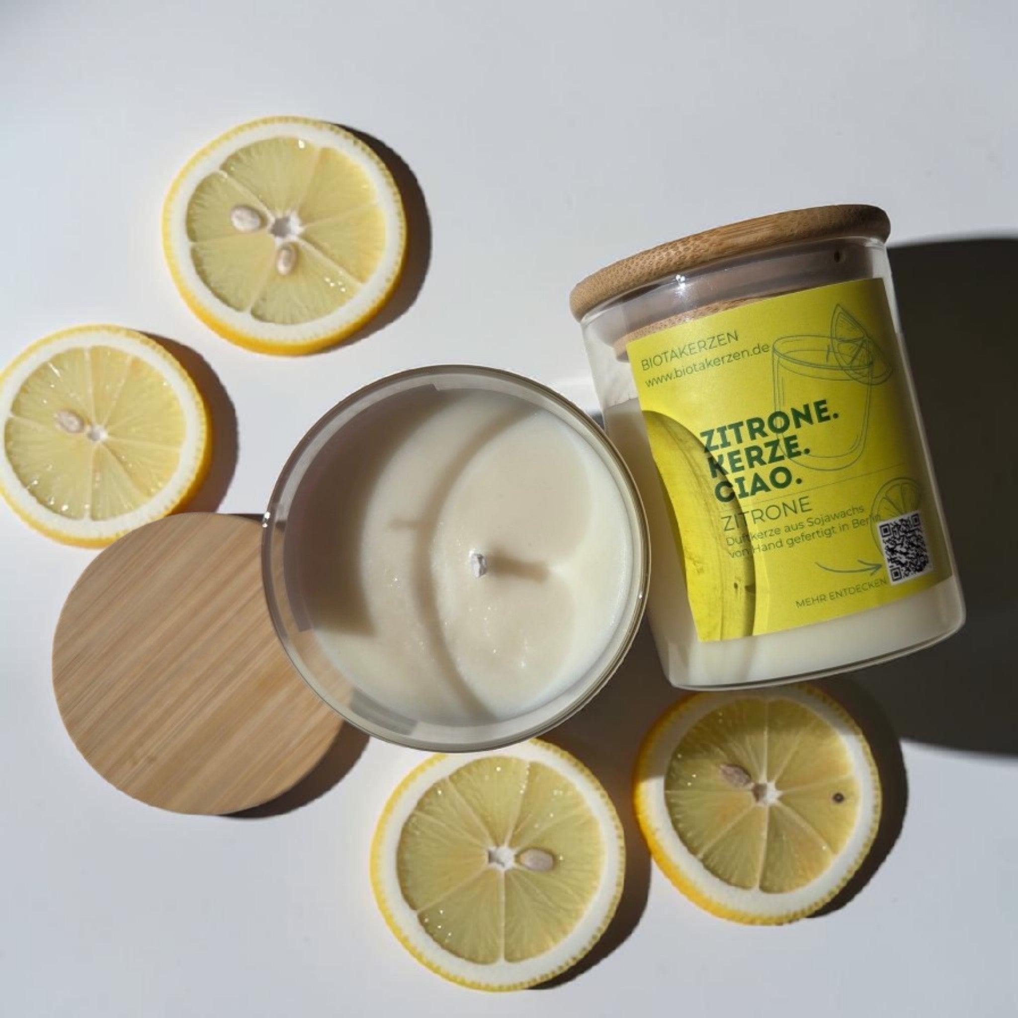 BiotaKerzen Zitronen-Duftkerze aus Sojawachs in einem geöffneten Glas mit weißem Wachs und Bambusdeckel, von oben fotografiert und mit Zitronenscheiben dekoriert