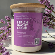 Duftkerze Flieder von BiotaKerzen aus der Kollektion Berlin macht Abend, im Glas mit Bambusdeckel, dekoriert mit lila Blüten.